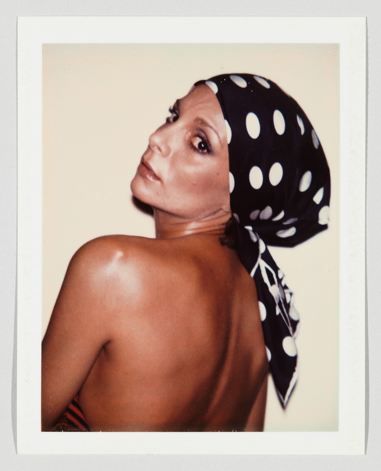 A woman looks over her shoulder wearing a black polka-dot headscarf with a bare back.