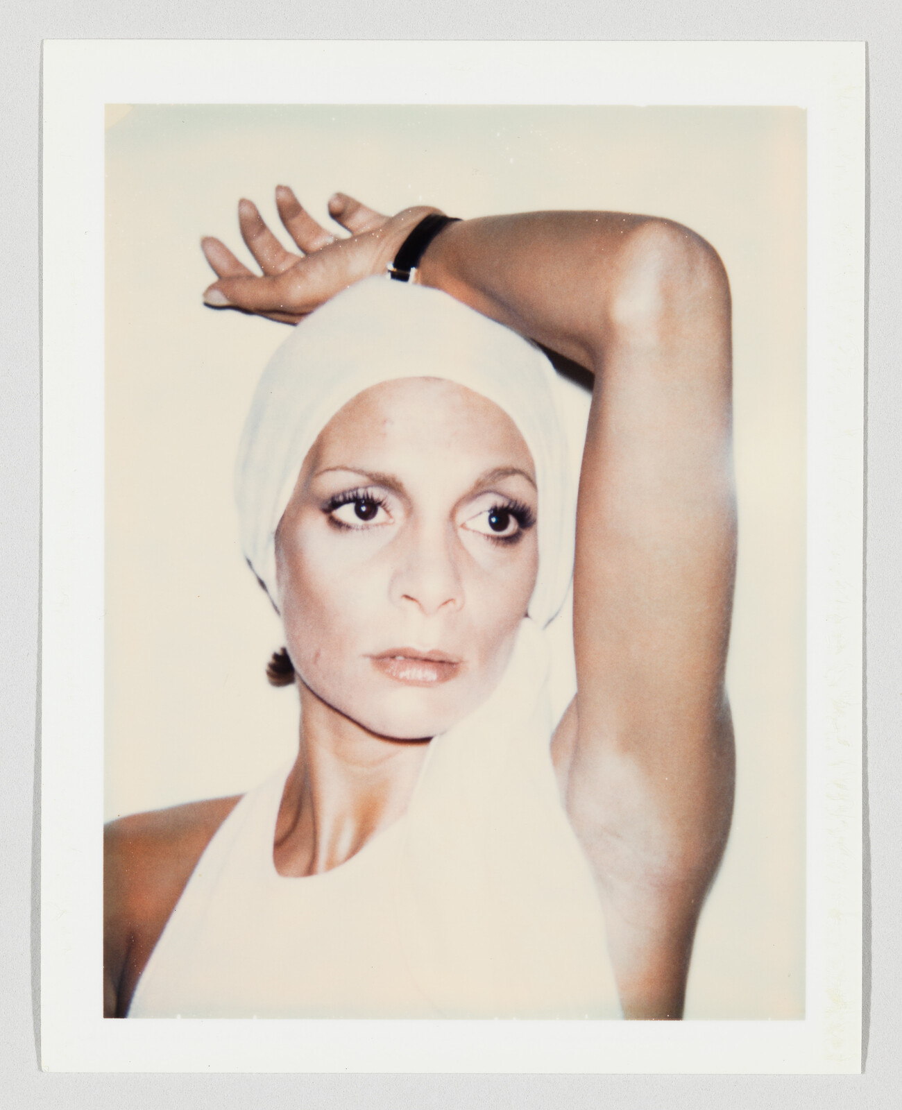 Woman wearing a white headscarf raises one arm above her head while looking to the side.