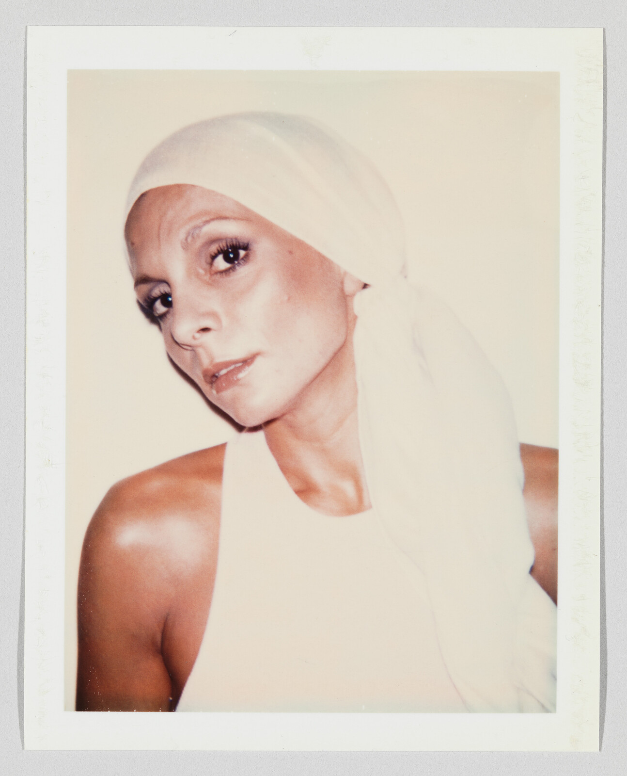 Woman wearing a white headscarf and sleeveless top looks directly at the camera with soft expression.