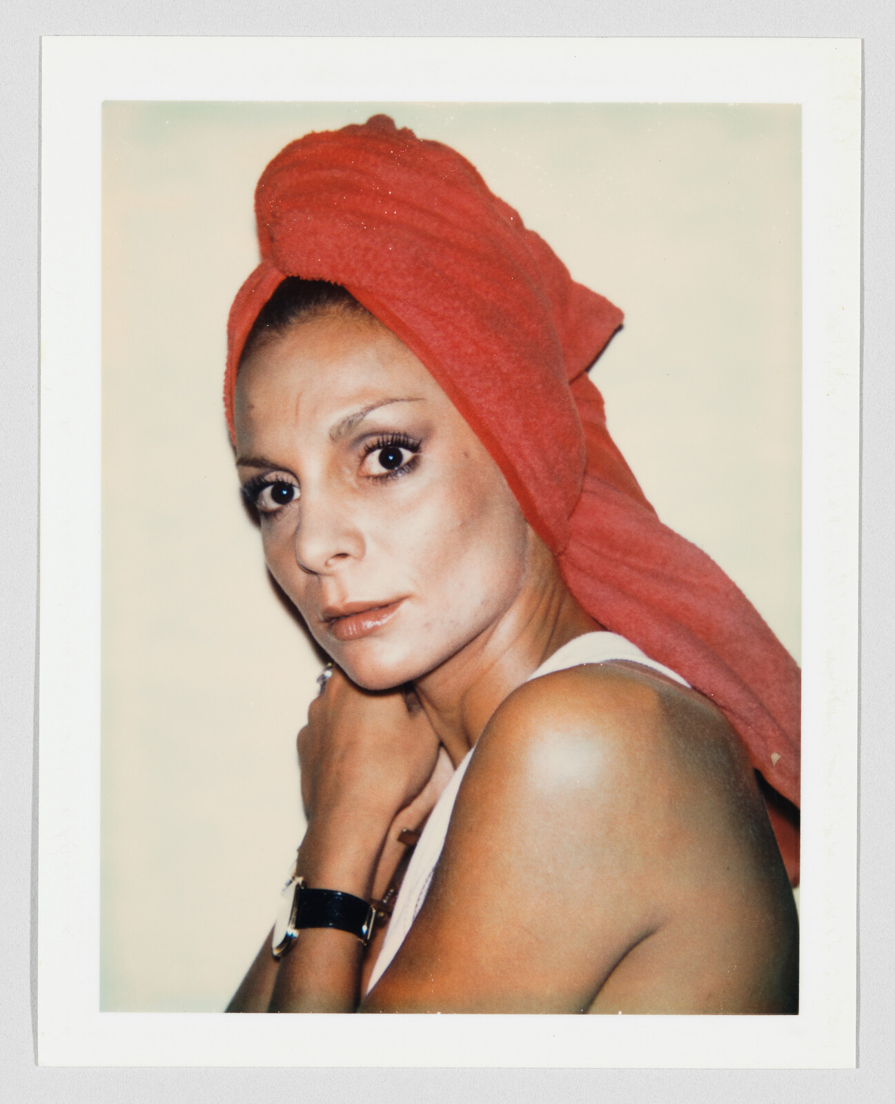 Woman with a red towel wrapped around her head looks at the camera, wearing a white top and watch.