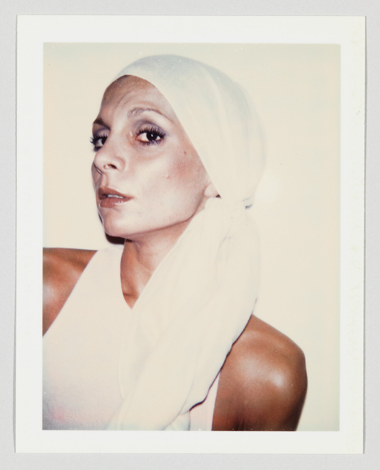 A woman wearing a white headscarf looks over her shoulder with a serious expression.