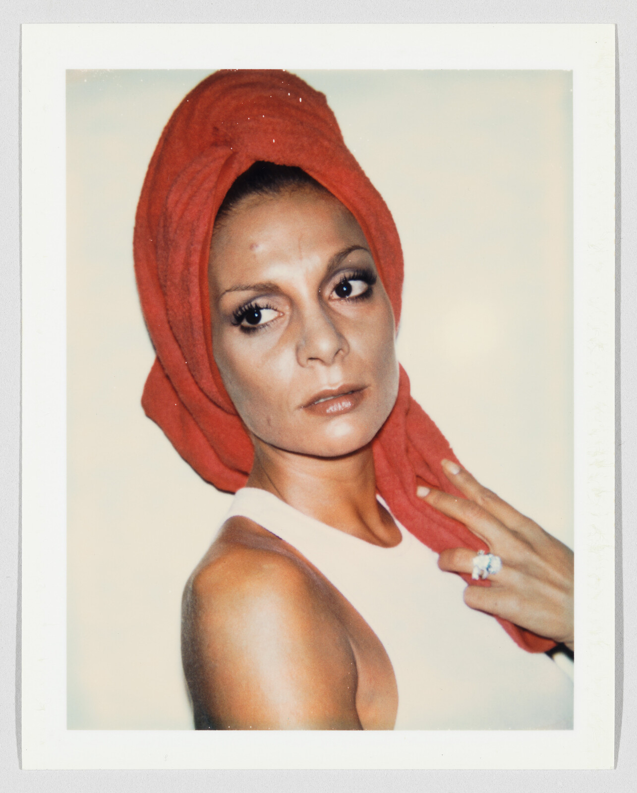 Woman wearing a red towel turban and white top looks sideways while touching a large ring.