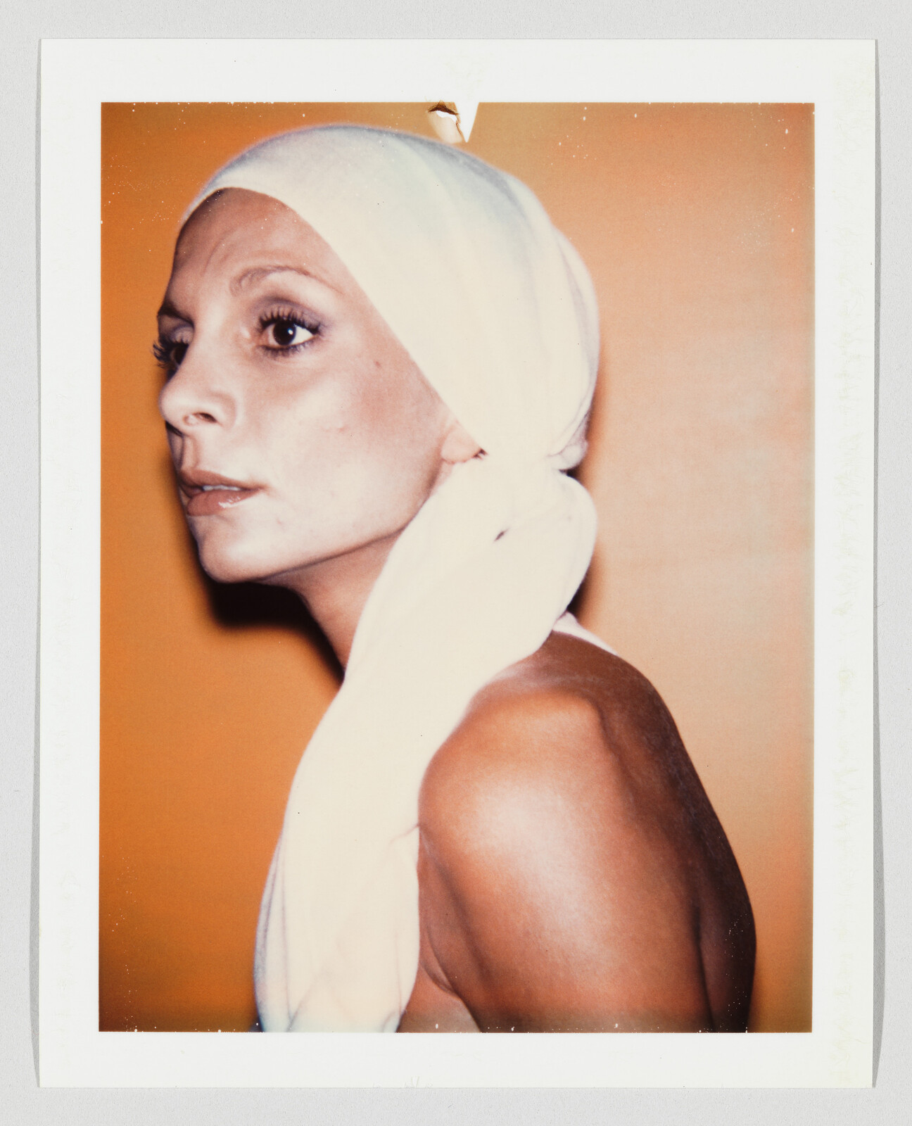 A woman with a white headscarf looks pensively to the left against an orange background.