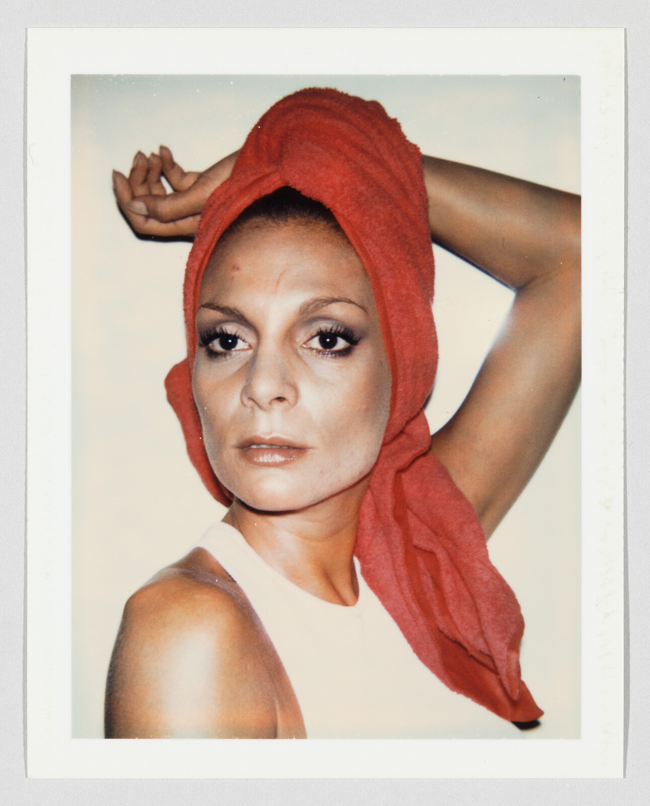 Person with a serious expression wears a red towel wrapped around their head and a sleeveless top.