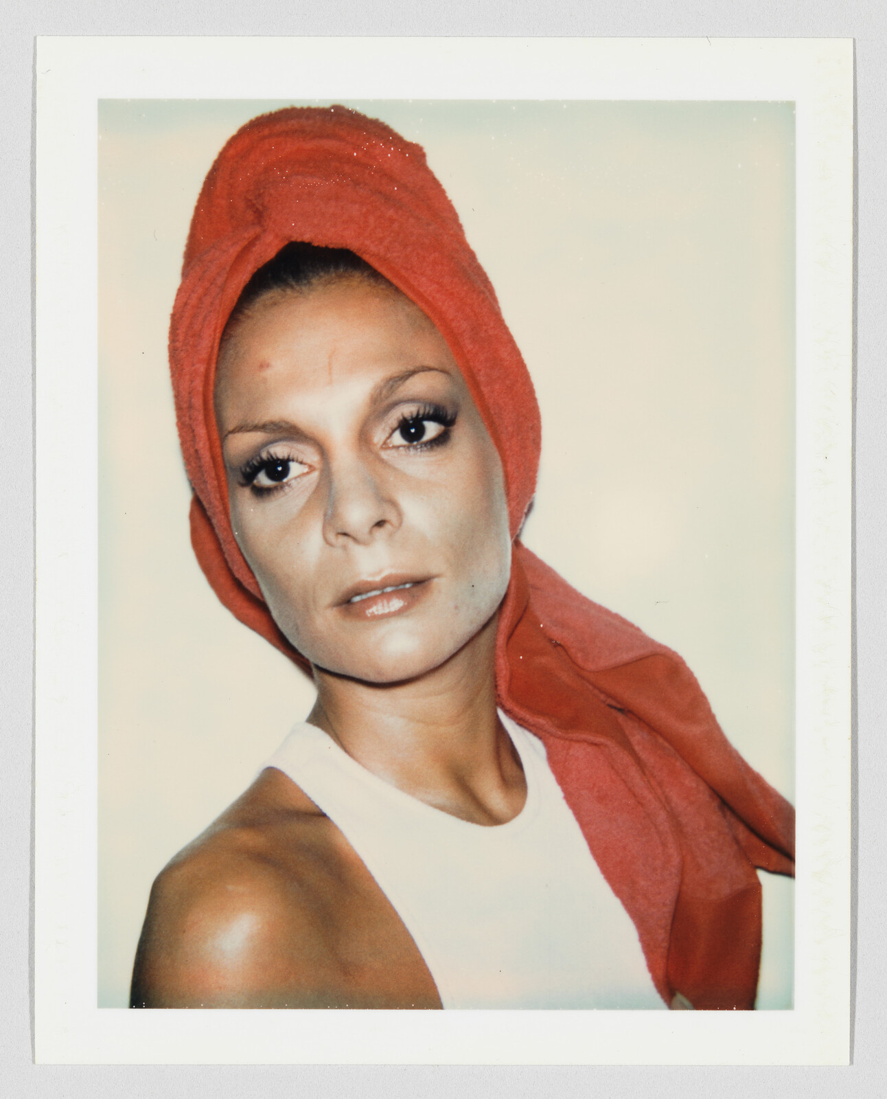 Woman wearing a red towel wrapped around her head and a white tank top, looking slightly off camera.