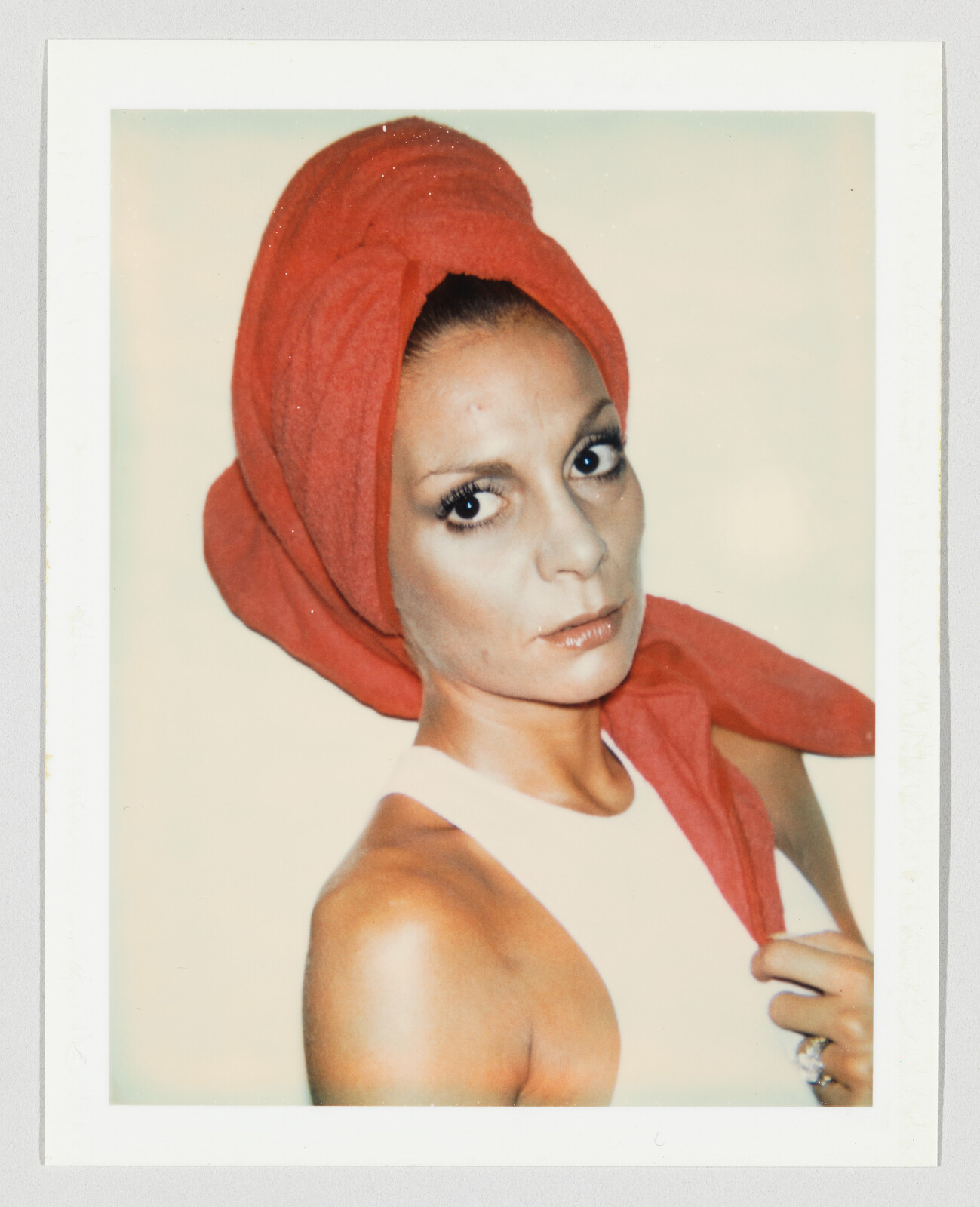 Woman with a red towel wrapped around her head looks directly at the camera while holding the towel.