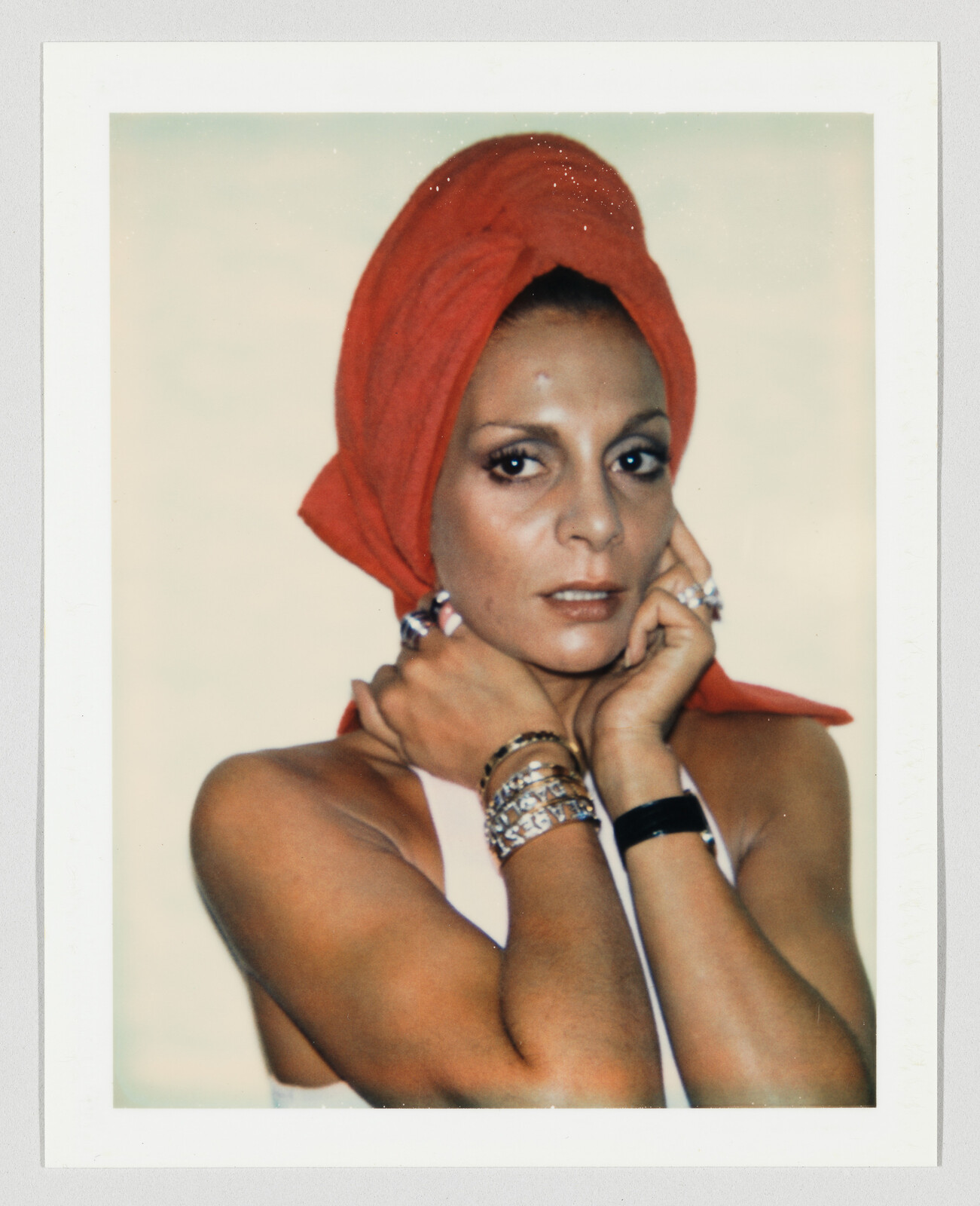 Woman wearing a red headscarf looks at the camera while holding her neck and face.