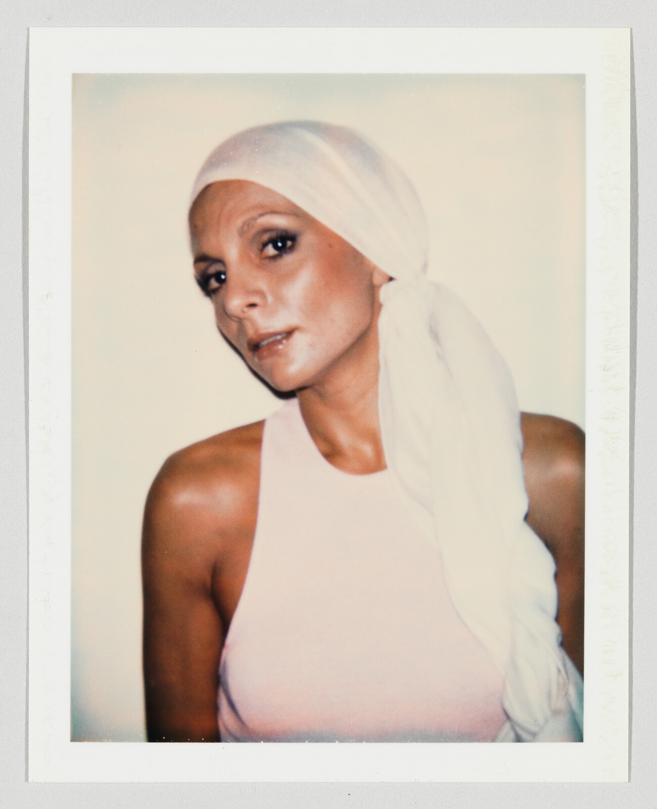 Woman wearing a white headscarf and pink sleeveless top looks toward the camera with a calm expression.