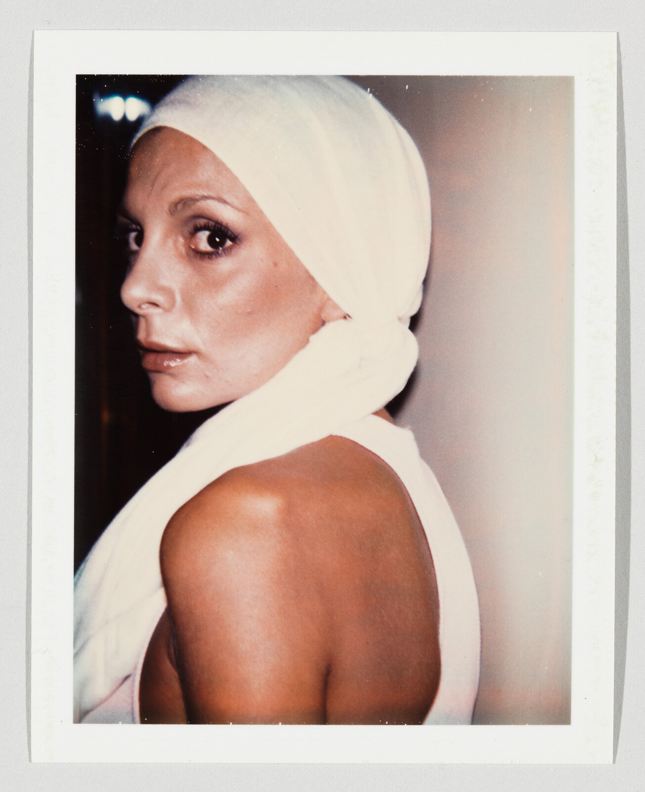 Woman wearing a white headscarf looks over her shoulder toward the camera.