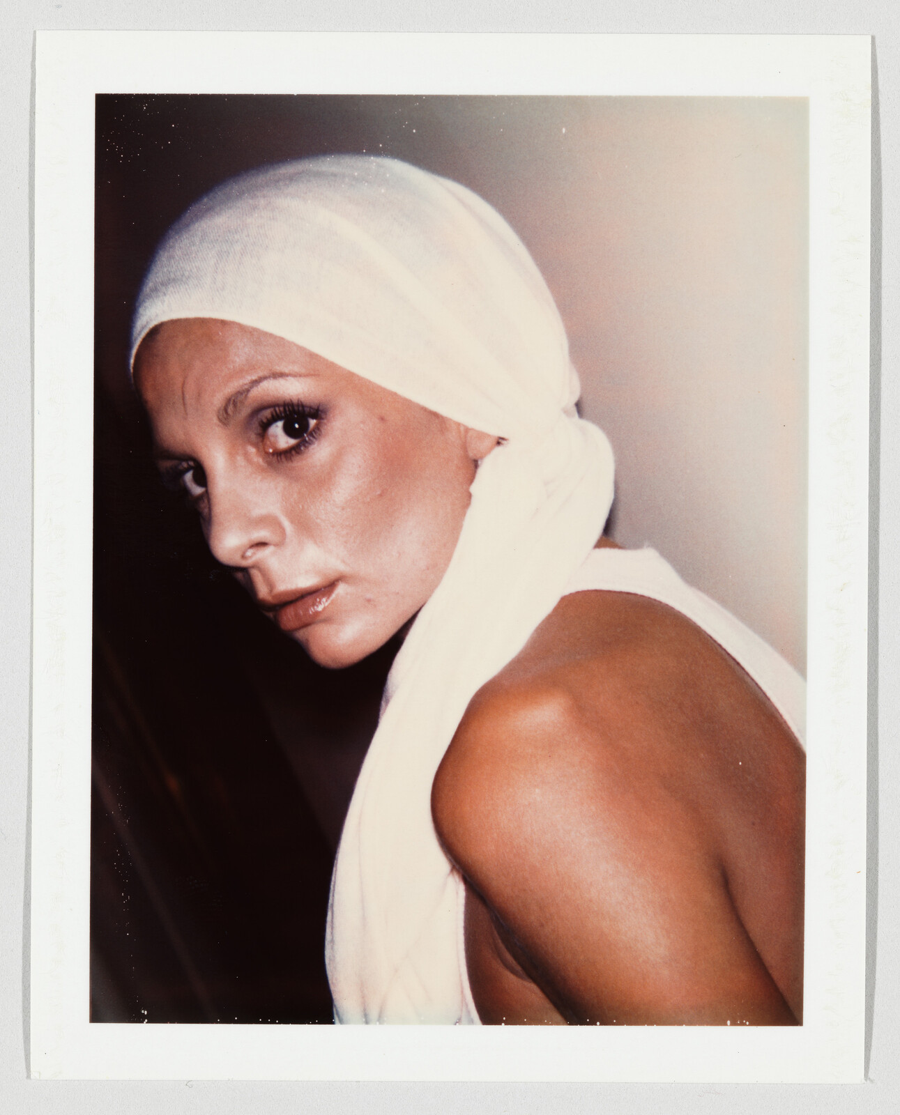 Woman wearing a white headscarf looks over her shoulder with an intense, focused expression.