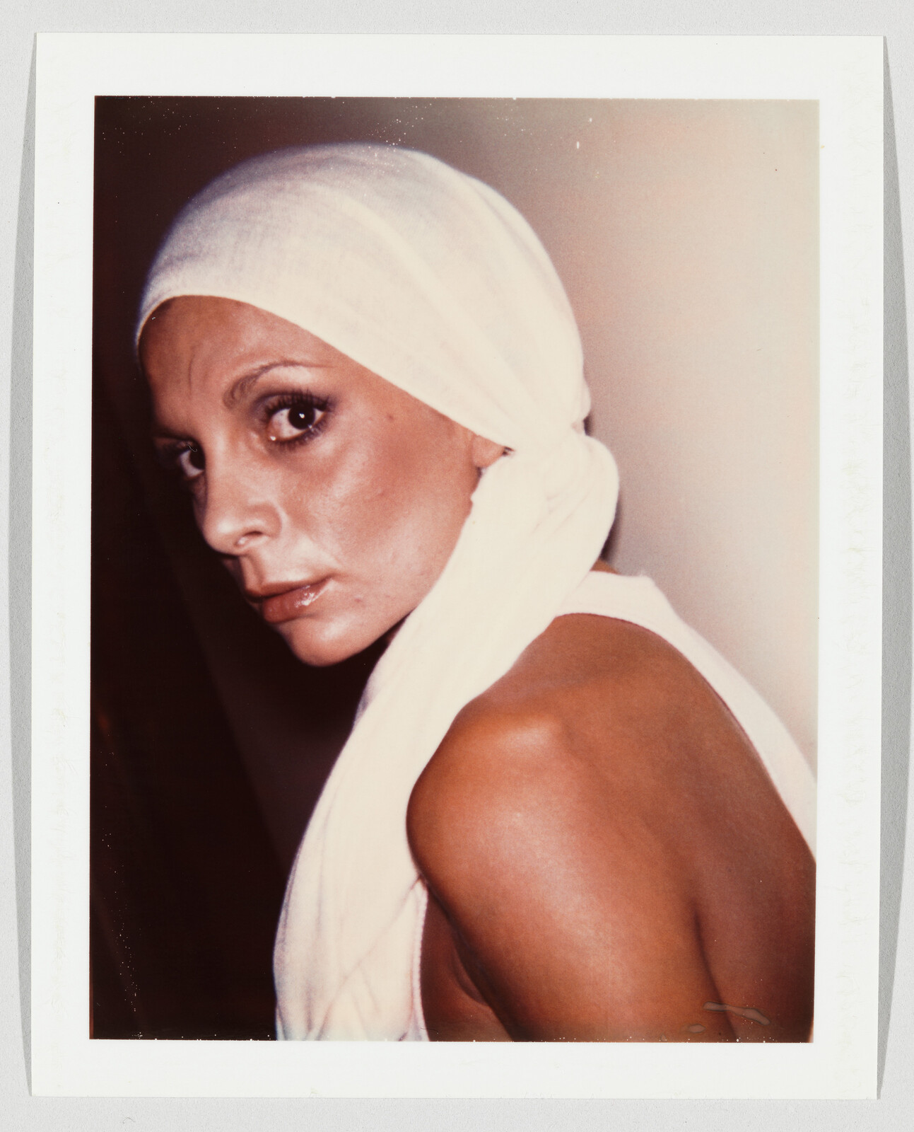 Woman wearing a white headscarf looks over her shoulder with a serious expression.