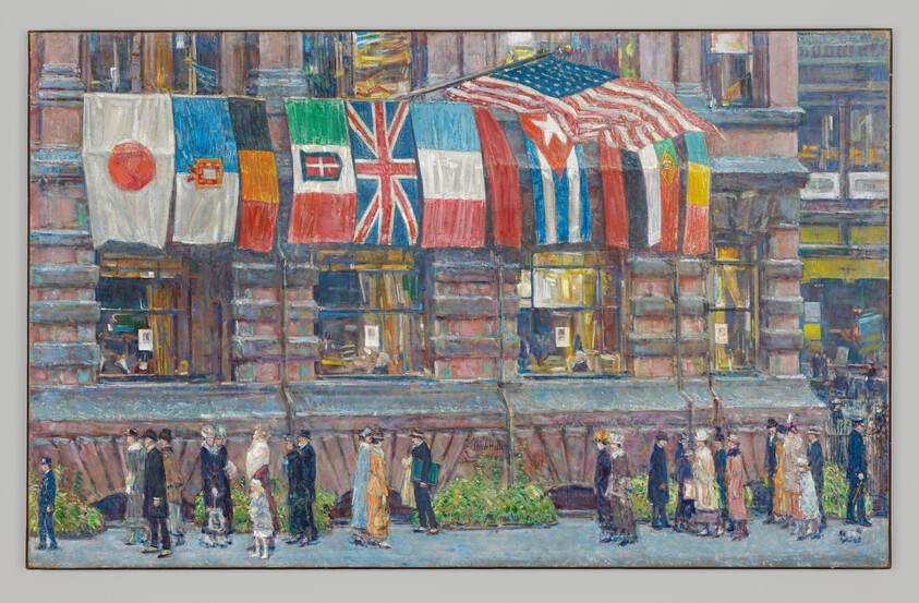 People walk past a city building draped with multiple national flags, including the American flag.