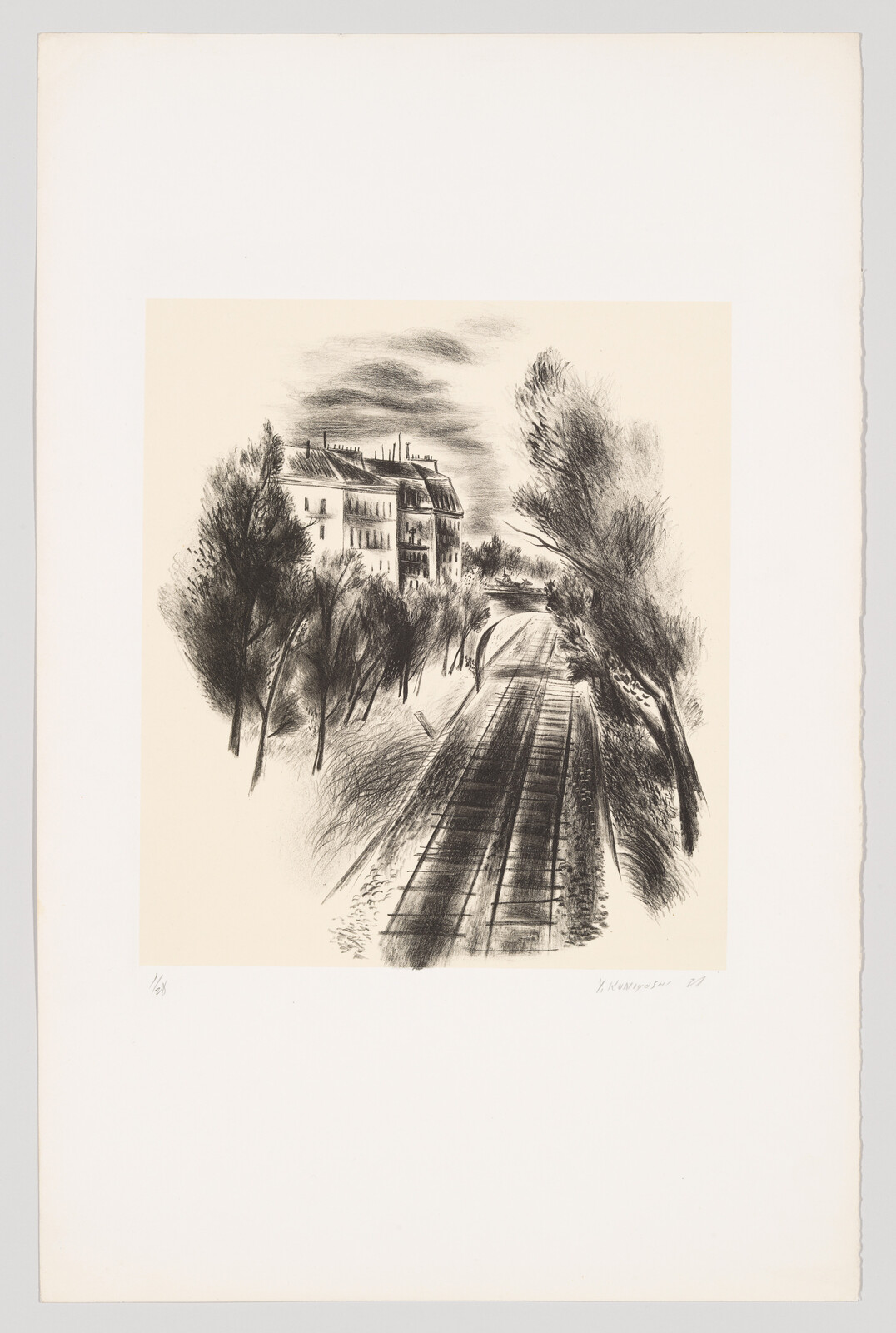 Railway tracks run past trees toward a large apartment building under a cloudy sky.