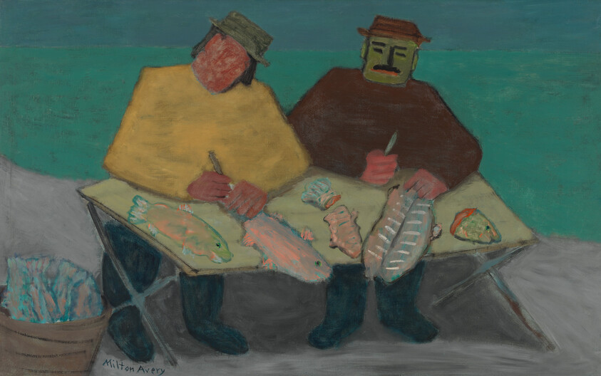 Two fishermen sit at a table by the shore cleaning several fish.