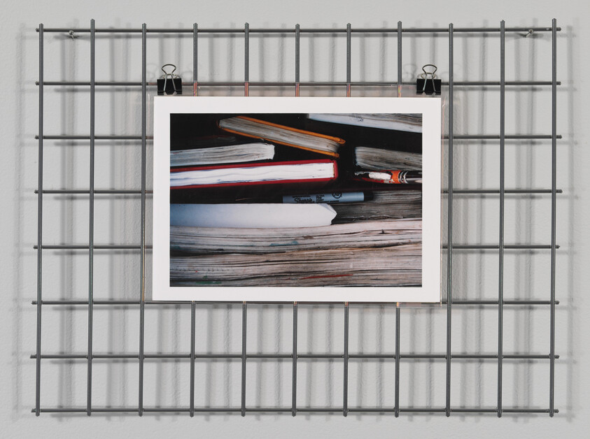 A metal grid holds a clipped picture showing a close-up of stacked notebooks and a marker.