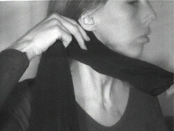 A person wraps a dark scarf or cloth around their neck, holding one end with their hand.