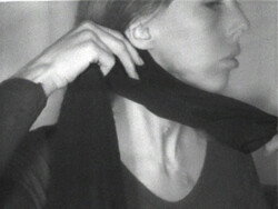 A person in profile adjusts a dark scarf around their neck with one hand.