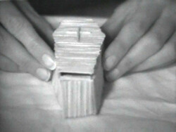 Two hands carefully stacking a pile of thin, rectangular objects, possibly cards or tiles, on a surface.