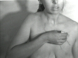 Woman with bare chest covering her breasts with one arm and looking off to the side.