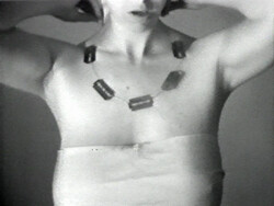 Person wearing a necklace made of small rectangular objects, with arms raised and torso wrapped in fabric.