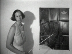 A woman stands next to a wall chart, pointing at it with a stick while explaining something.