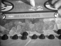 A box labeled "Mexican Hats" candy is held above several small, hat-shaped candies on a table.