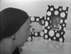 A person wearing a headscarf looks at two framed animal photos with polka dot borders on a table.