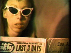 Person wearing white cat-eye sunglasses reads a newspaper with a visible headline: "LAST 3 DAYS."