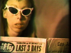 Person wearing white cat-eye sunglasses reads a newspaper with a visible headline: "LAST 3 DAYS."