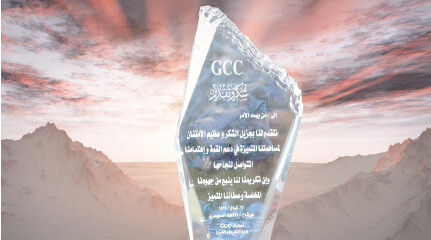 A glass award with Arabic and English text, labeled "GCC," stands in front of a mountain background.