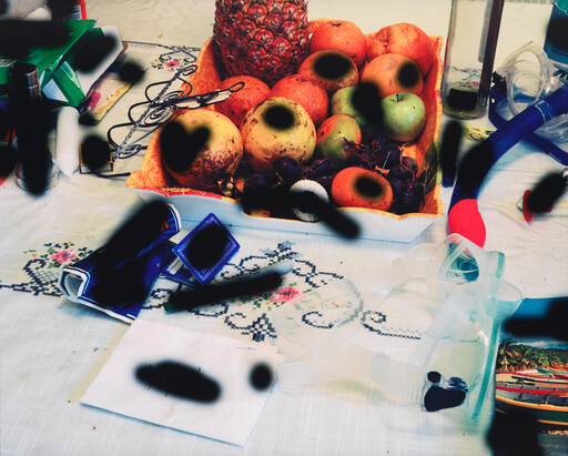 A bowl of assorted fruit sits on a cluttered table beside snorkeling goggles and small items.