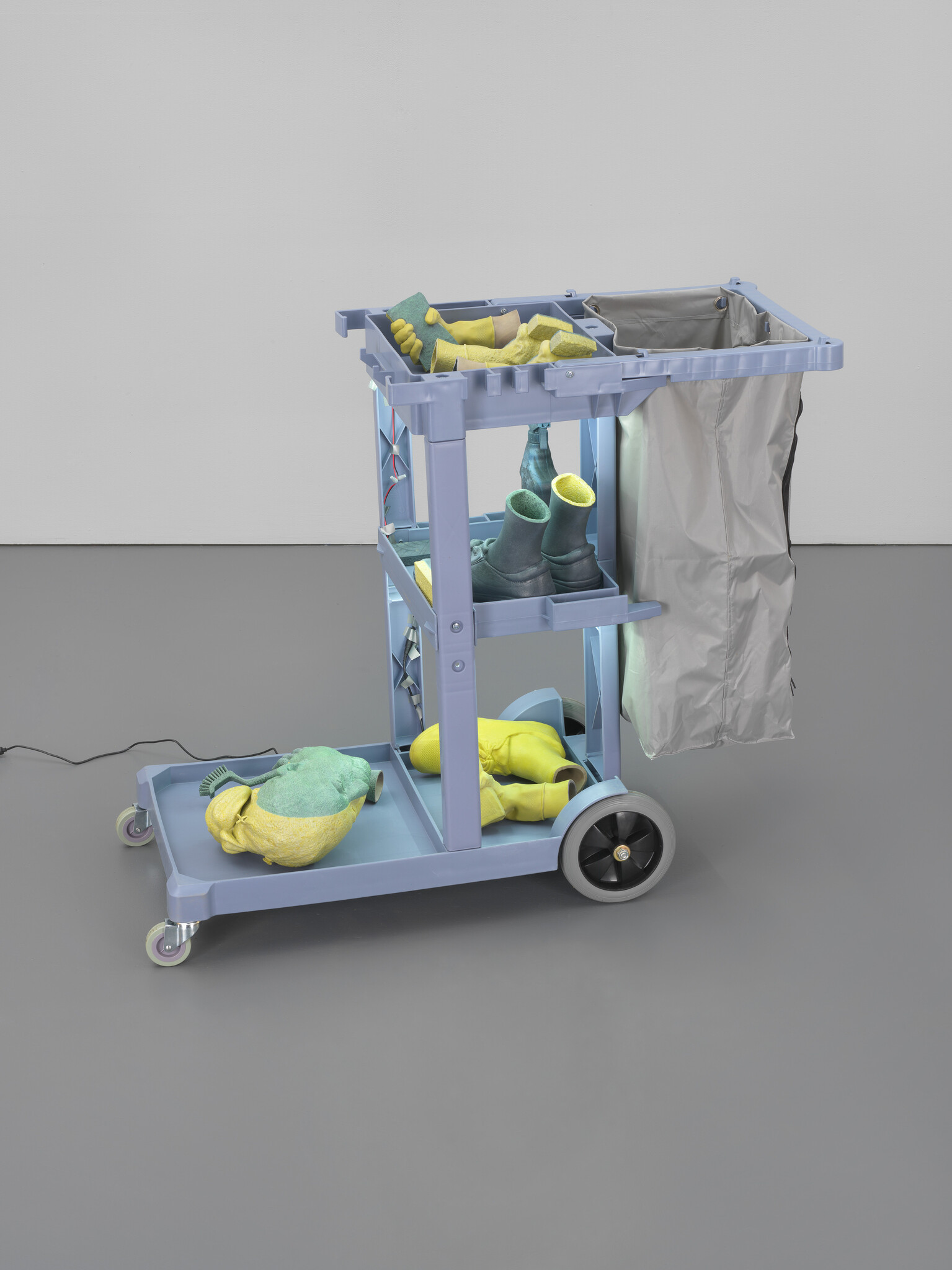 A blue janitor cart holding rubber gloves, cleaning sponges, boots, and a gray trash bag.