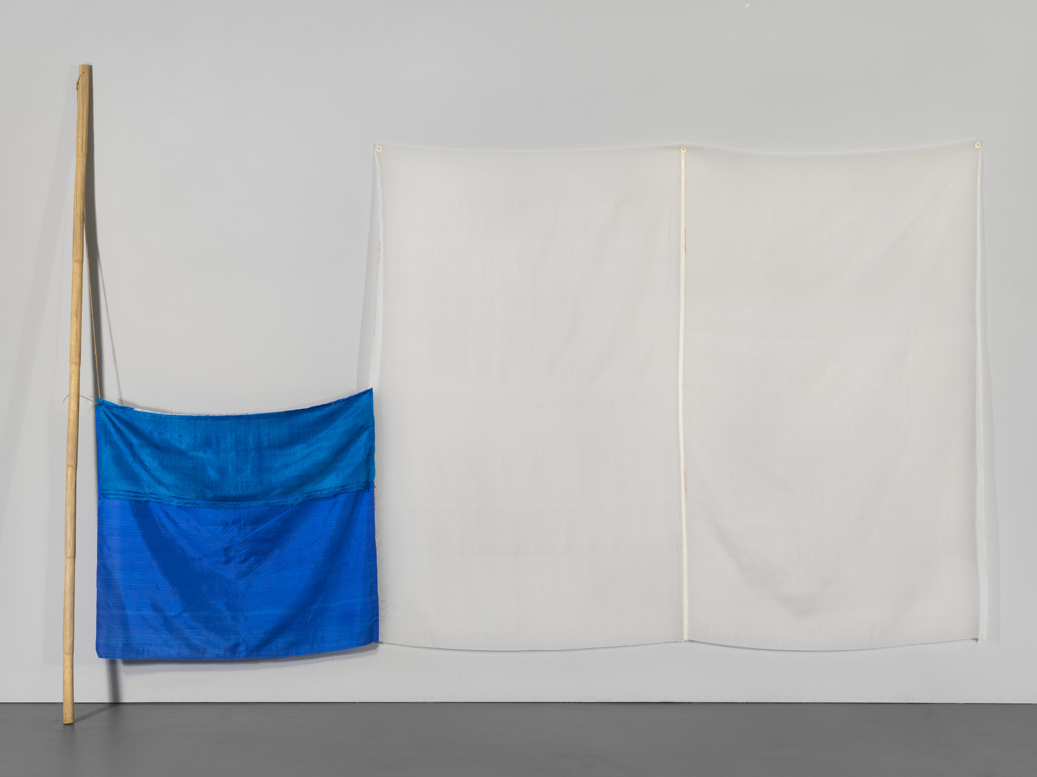 A blue cloth hangs from a wooden pole beside a large white fabric panel pinned to the wall.