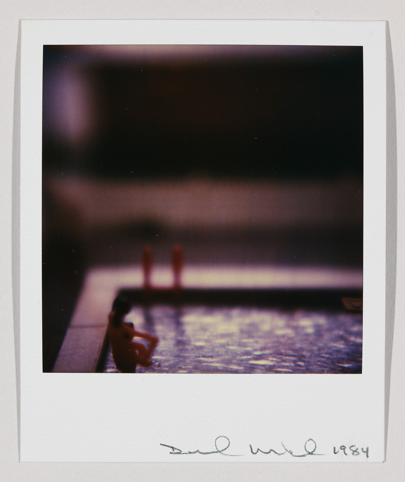 A person sits at the edge of a dimly lit pool in a blurred Polaroid-style photograph.