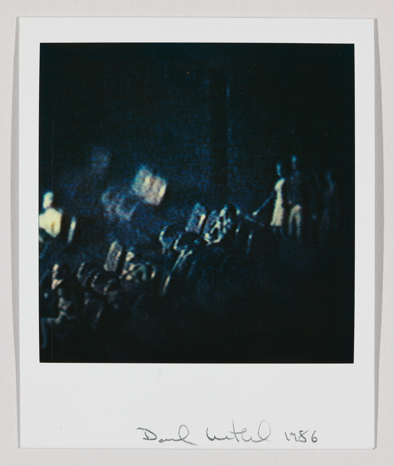 Blurry dark photograph showing a dimly lit crowd or audience with scattered bright highlights.