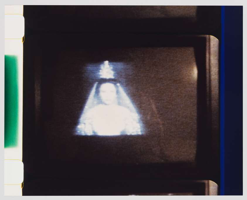 A small CRT screen displays a bright, blurred figure wearing a crown and veil like a religious statue.