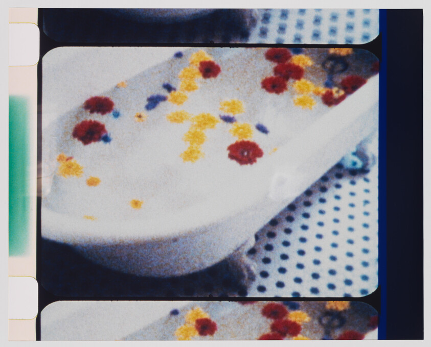 White bathtub filled with foam and scattered red and yellow flower petals on a polka-dot floor.