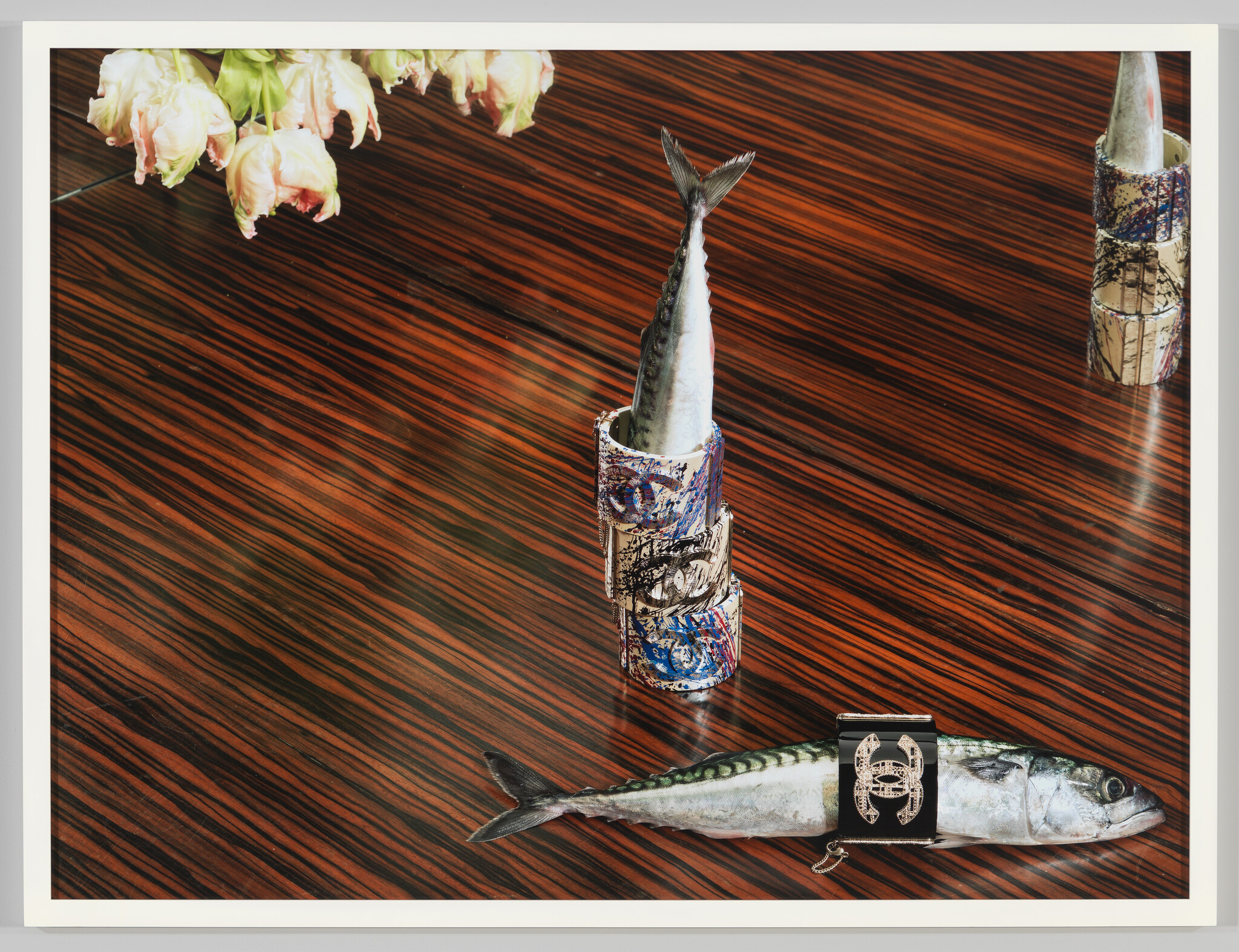 Two mackerel on a striped wooden table, one standing in stacked cans and one strapped with a decorative band.