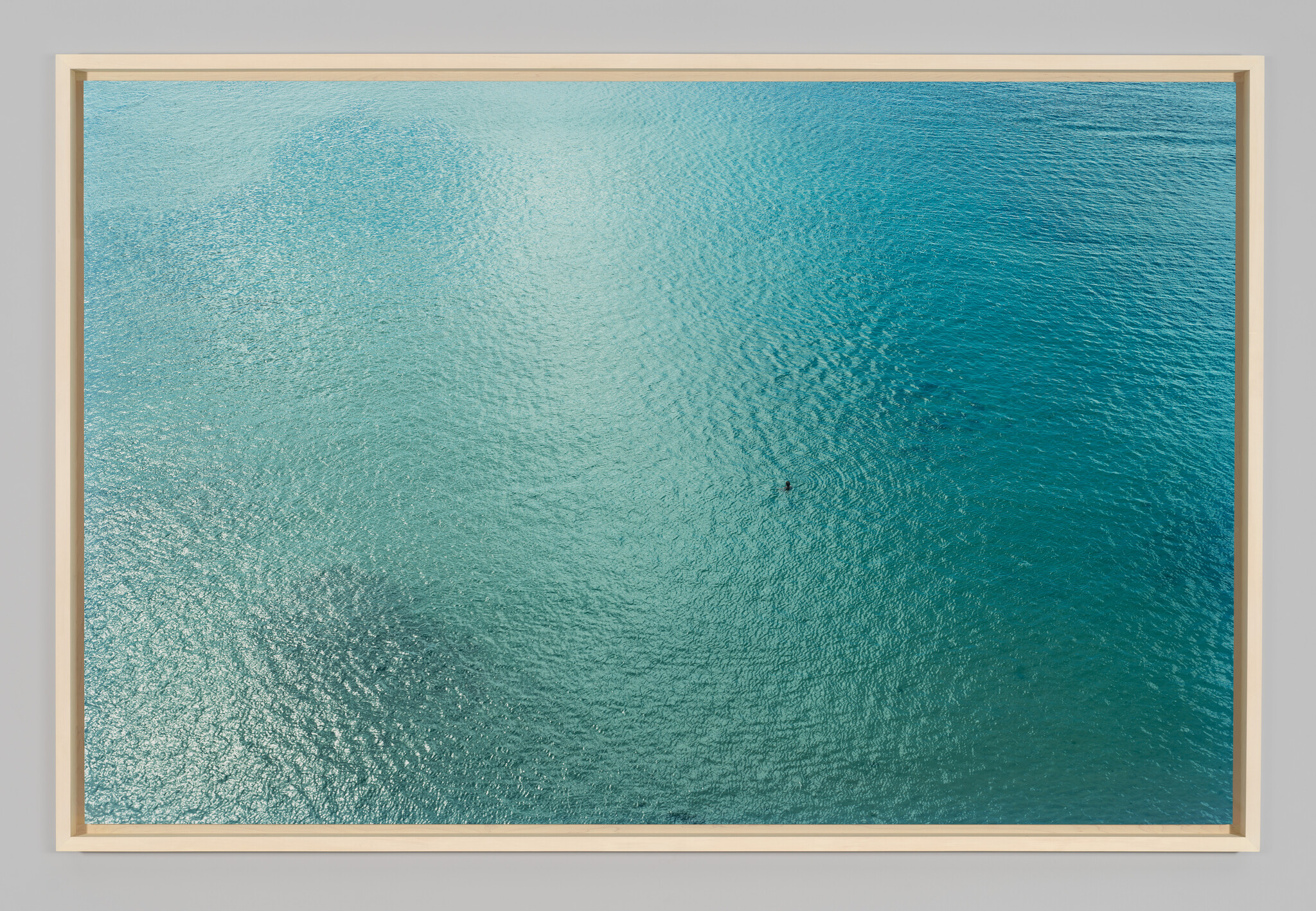 A lone swimmer floats in the vast turquoise ocean seen from above.