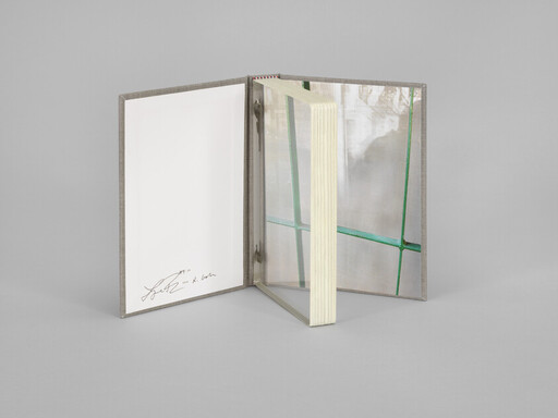 An open notebook with a reflective inner cover and stacked pages standing upright, signed on the left page.