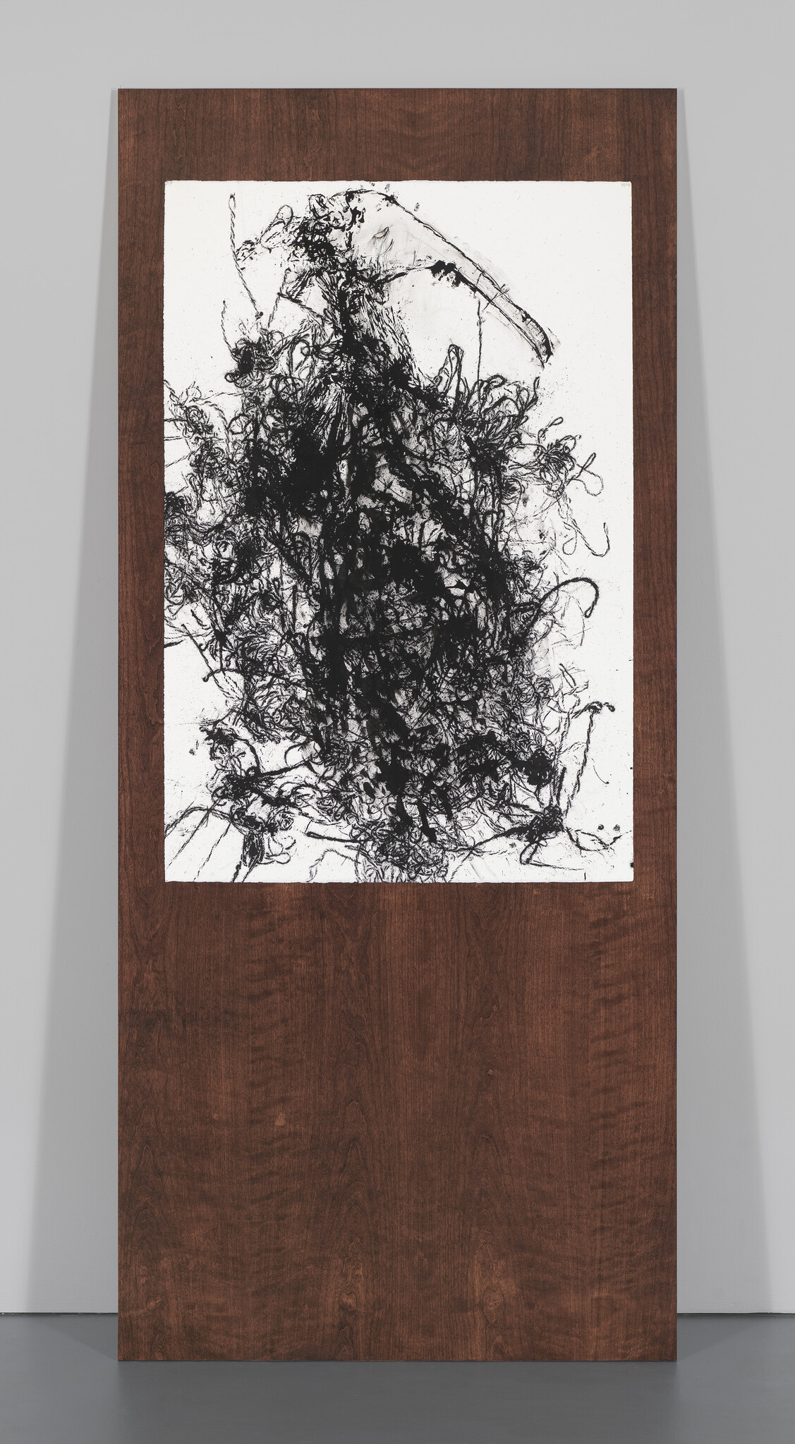 Large abstract black ink tangle on white paper mounted high on a tall wooden panel.