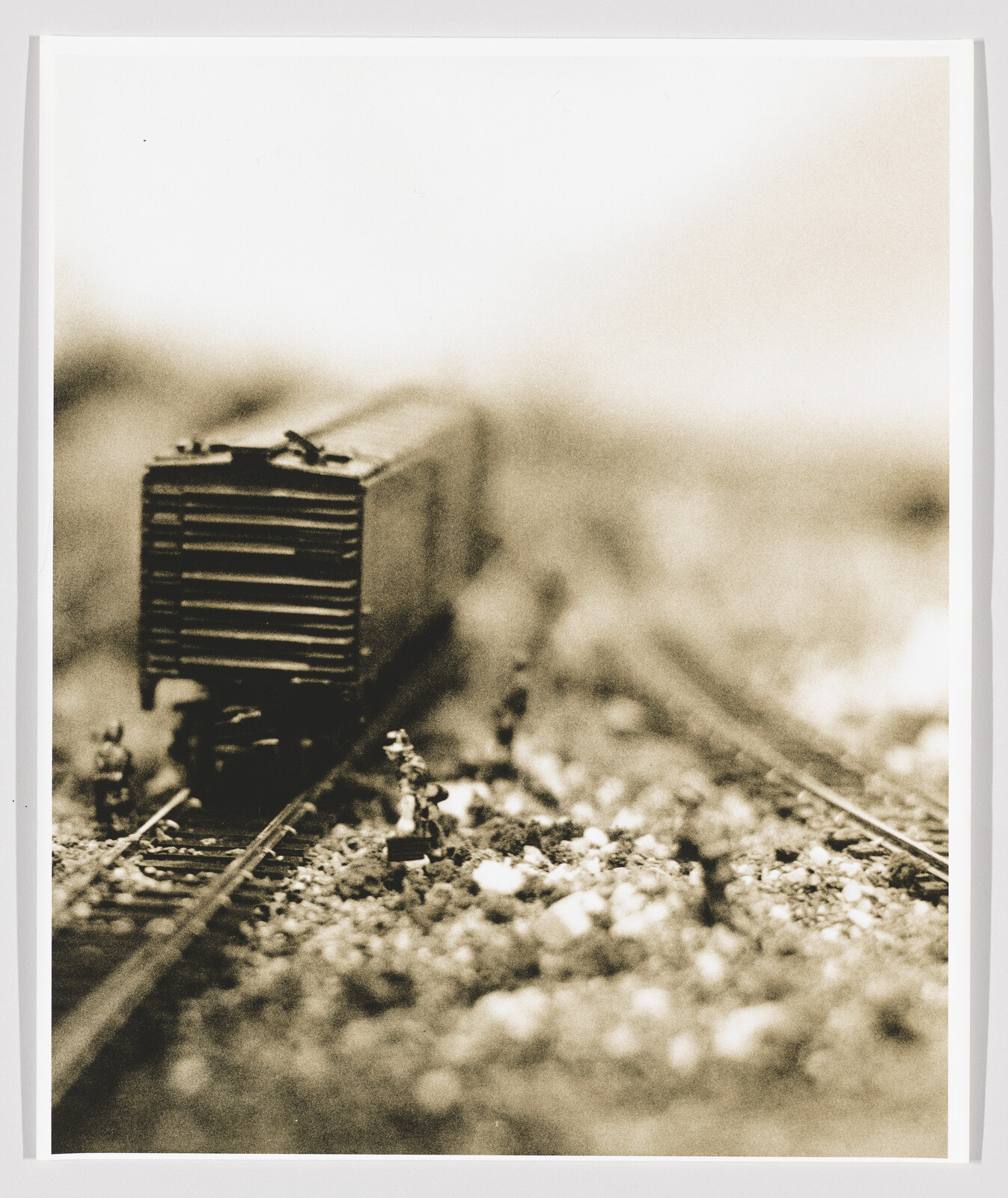 Miniature boxcar sits on model train tracks while tiny figures stand and work nearby.