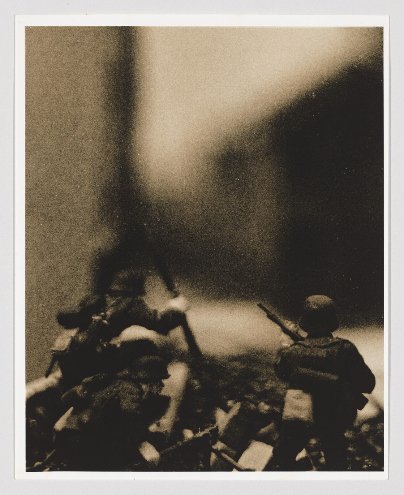 Small toy soldiers advance over rubble with rifles in a grainy sepia scene.