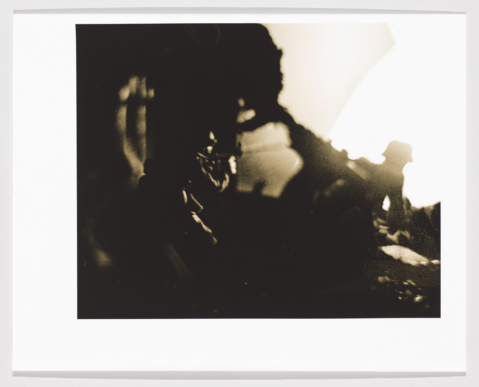 A monochromatic photograph with high contrast and blurred silhouettes, possibly depicting figures or objects with indistinct shapes against a lighter background. The image has a vintage or artistic quality, with the focus and composition leaving the subject matter open to interpretation.