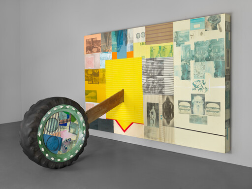 A large wooden beam mounted on a painted wheel leans into a colorful wall-mounted collage.