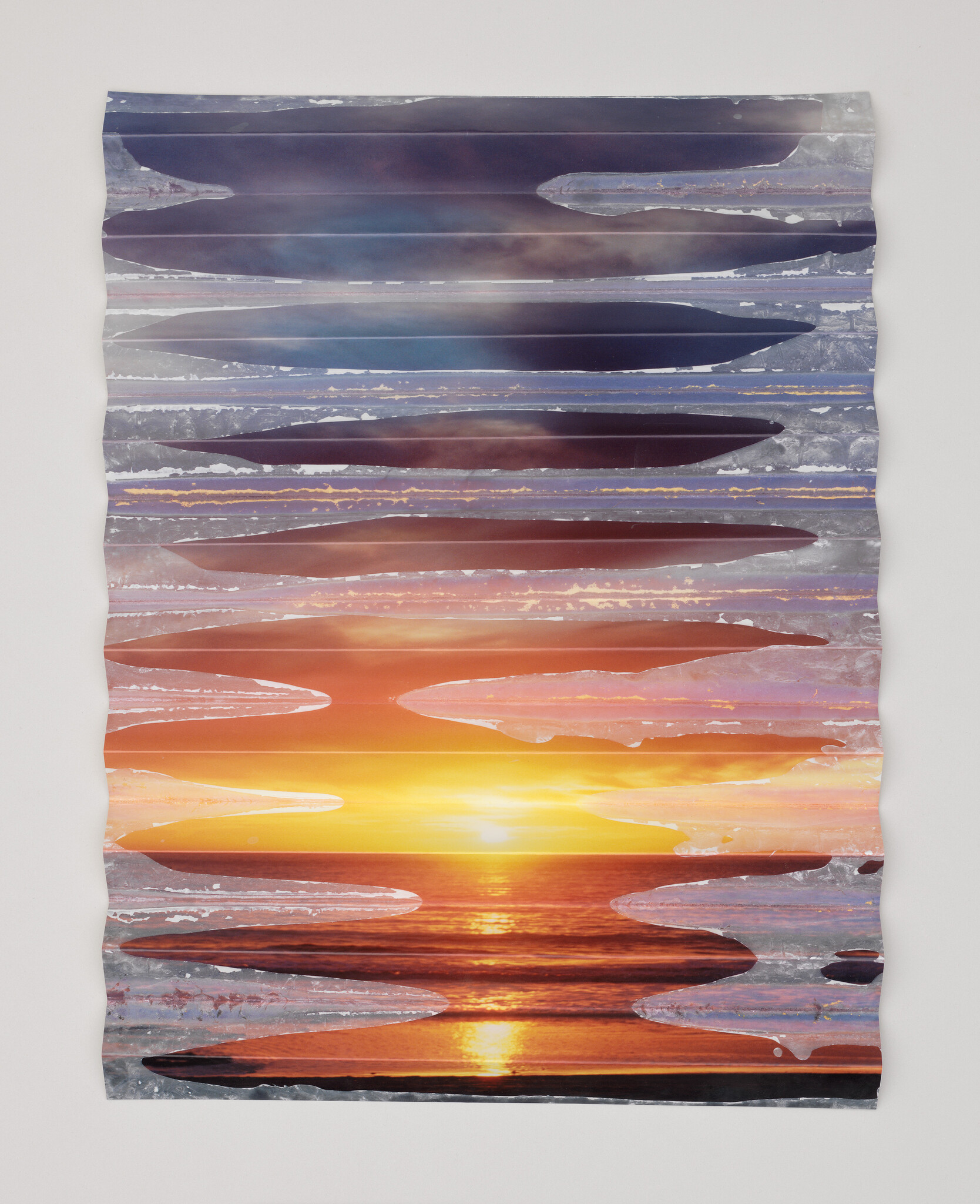 Corrugated metal panel with horizontal cutouts revealing a colorful sunset over the ocean.