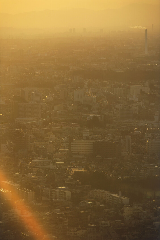 City skyline covered in golden haze with a distant smokestack releasing white smoke.