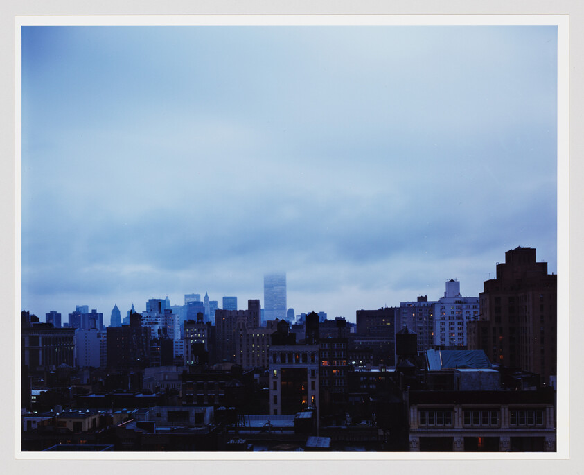 A city skyline during twilight with a mix of low and high-rise buildings under a cloudy blue sky.