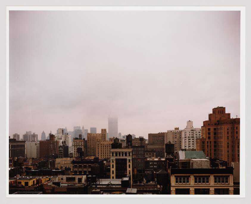 City skyline with low fog obscuring taller skyscrapers above densely packed mid-rise buildings.