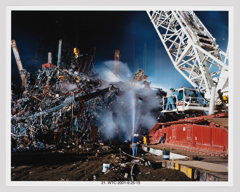Rescue workers spray water on smoldering World Trade Center rubble beside a large crane.